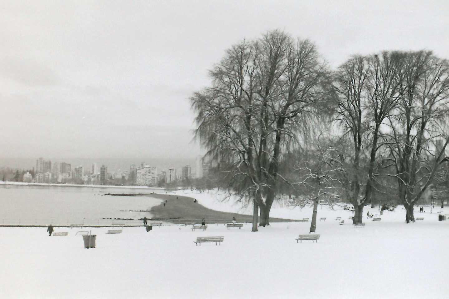 A black and white photograph of a snowy beach in winter with a city in the background.