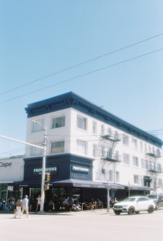 Blue sky, blue and white building on the corner. White car glowing